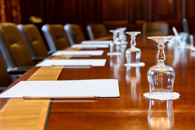Close-up of a conference table set for a meeting. Papers, pencils, and inverted glasses are neatly arranged on a glossy, wooden surface.